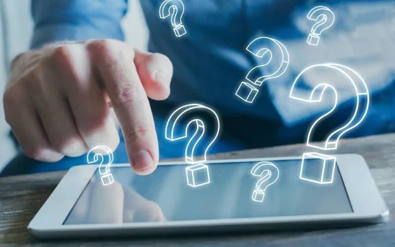 Person interacting with a digital tablet surrounded by question marks, symbolizing frequently asked questions, support, and information resources.