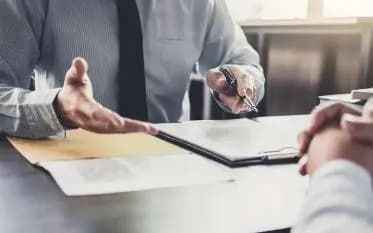 Business professional discussing documents across a desk, representing organizational policies, terms, guidelines, and compliance information.